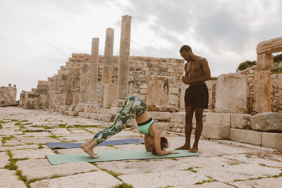 A man instructs a woman in yoga at ancient ruins, promoting fitness and mindfulness.